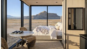A bedroom with a large window, a bed, a round table, and a woven chair. - Reflections (Torrey)