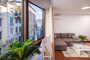 Ein modernes Wohnzimmer mit großem Fenster, einem grauen Sofa, einem kleinen Tisch und einem Blumentopf.
