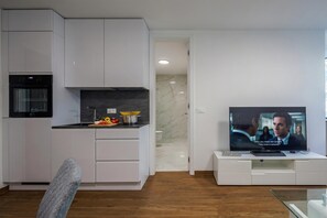 A modern kitchen with white cabinetry, a built-in oven, and a dining area with a TV. - Luxury City Apartment Adialuxe S4, Rijeka, Croatia (Rijeka)