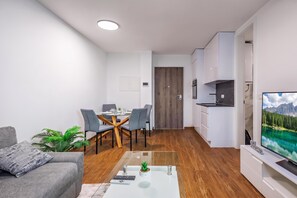 Ein modernes Wohnzimmer mit einem Glastisch, einem grauen Sofa und einem Flachbildfernseher.