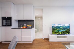 Una cocina moderna con armarios blancos, horno empotrado y comedor con mesa y sillas de madera.