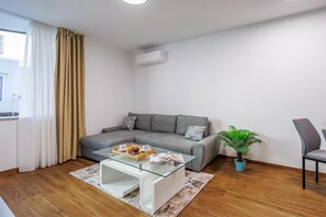 Ein modernes Wohnzimmer mit einem grauen Sofa, einem Glastisch mit einer Muffinsplatte, einer Topfpflanze und einem Sessel.