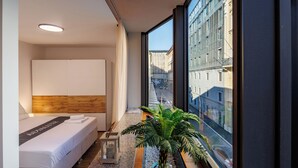A modern hotel room with a large window, a bed, a bedside table, a potted plant, and a small decorative item. - Luxury City Apartment Adialuxe S4, Rijeka, Croatia (Rijeka)