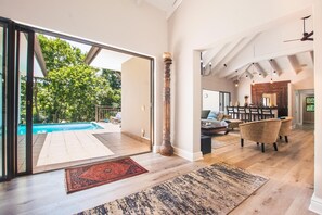 Un vaste espace de vie comprenant une piscine, un coin repas et une cuisine dotée de hauts plafonds et de poutres apparentes.
