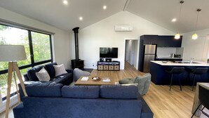 Ett modernt vardagsrum med en soffa, ett soffbord och en tv. Det finns också ett köksområde med ett kylskåp och en bardisk.