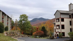 Un bâtiment doté d’un mur de soutènement en pierre, d’un parking et ayant une chaîne de montagnes en arrière-plan.