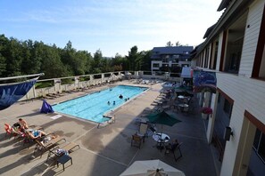 A rooftop pool area with lounge chairs and umbrellas, surrounded by a building with a white facade and a view of trees. - Wonderful 2-Bedroom Condo Located at Pollard Brook (Lincoln)