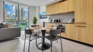 A modern kitchen with wooden cabinets, a dining area with a round table and chairs, and a large window with a city view. - 501 First Luxury 1 BR + Den & 2 Baths Rooftop Pool & GYM 502 (Miami)
