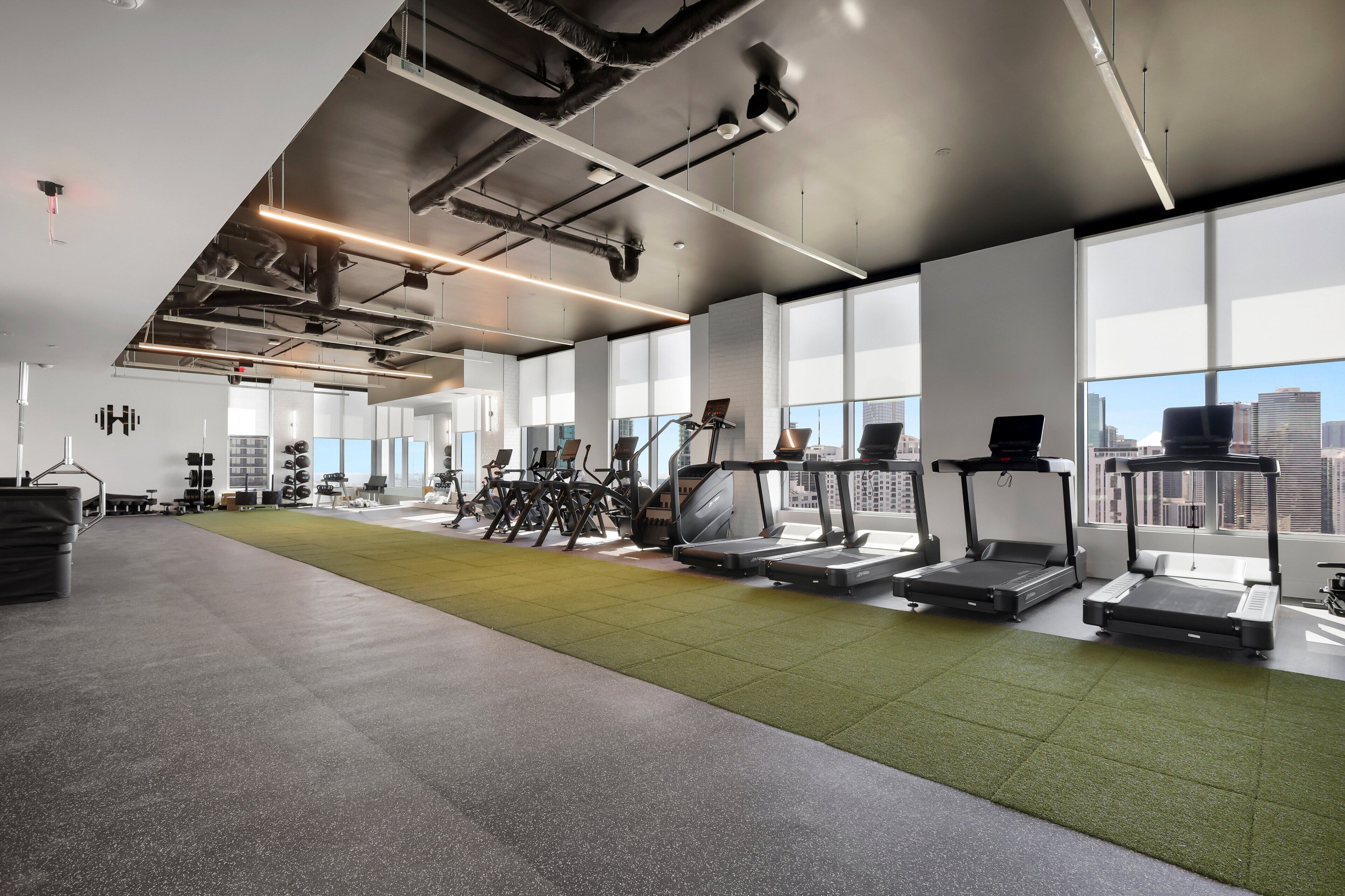 A modern gym with exercise equipment, large windows, and a city view.