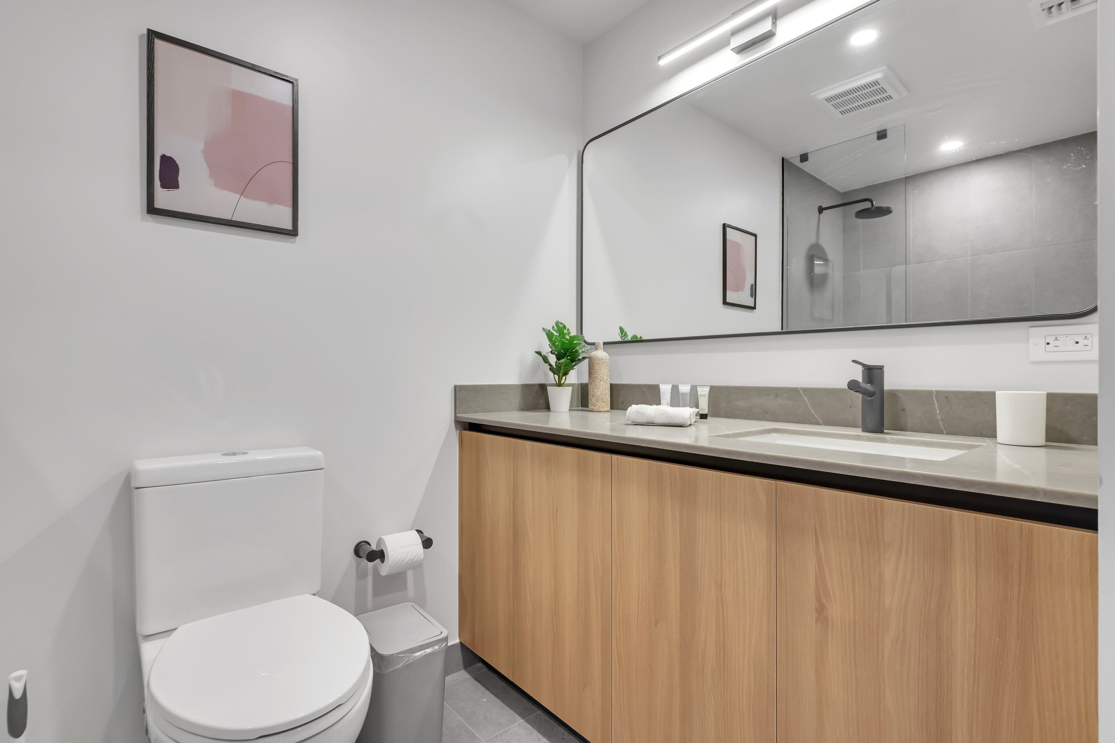 Une salle de bain moderne comprenant des toilettes, un lavabo, un miroir et une œuvre d’art abstraite encadrée accrochée au mur.