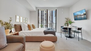 Une chambre moderne comprenant un lit, des tables de chevet, un bureau, des chaises et une grande fenêtre donnant sur la ville.