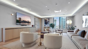 Un salon moderne doté d’un téléviseur à écran plat, d’un canapé, d’une table basse et d’une grande fenêtre offrant une vue sur les gratte-ciel.