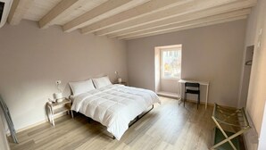 Quarto com cama, mesas de cabeceira, uma cadeira, janela e escrivaninha.
