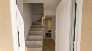 Um corredor com escadas que levam a um quarto, uma porta à direita e vista para outro cômodo.