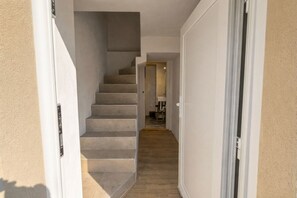 Ein Flur mit einer Treppe zu einem Zimmer, einer Tür rechts und einem Blick in ein weiteres Zimmer.
