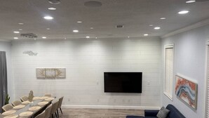 A modern living room with a dining area, a flat-screen TV mounted on the wall, and a blue sofa. - Sunset cruiser close to Redington Beach (Seminole)
