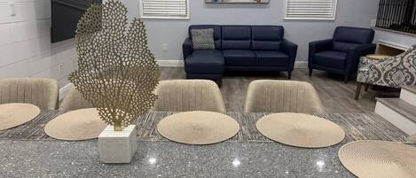 A modern living room with a grey marble table, beige woven placemats, a decorative tree sculpture, and a blue sofa set.