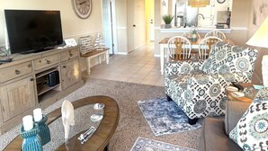 A living room with a TV, wooden furniture, patterned sofa, dining table, and kitchen in the background. - Close to everything! 1bdr in St. Pete beach (St. Petersburg)