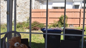 Een overdekt terras met rieten meubilair, een glazen tafel met een bloevas en een teddybeer op een stoel.