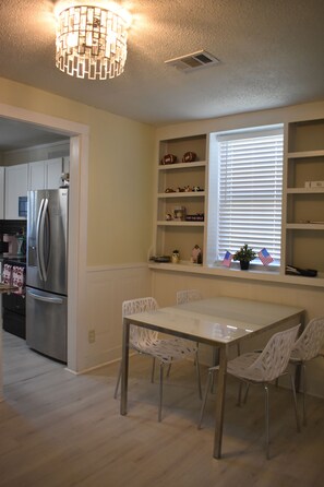 A kitchen with a stainless steel refrigerator, a dining table with four chairs, and a window with blinds. - 2-Bed Home Near Masters in Augusta, GA (Augusta)