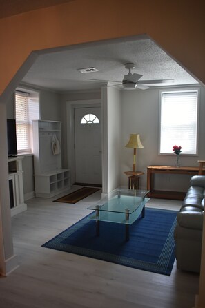 A room with a glass coffee table, a ceiling fan, a white door, and a window with blinds. - 2-Bed Home Near Masters in Augusta, GA (Augusta)