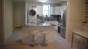Een keuken met een centraal eiland, barstoelen, een wasmachine en een koelkast.