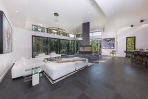 A modern living room with a fireplace, large windows, and a high ceiling. - Steps to slopes; 7,000 sq feet of Luxury, golf simulator, hot tub! (Copper Mountain)