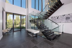 A modern interior with a glass staircase, a bench, and a view of the outdoors. - Steps to slopes; 7,000 sq feet of Luxury, golf simulator, hot tub! (Copper Mountain)