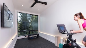 A room with a stationary bike, a window with a view of trees, and a bench with weights. - Steps to slopes; 7,000 sq feet of Luxury, golf simulator, hot tub! (Copper Mountain)