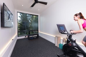 A room with a stationary bike, a window with a view of trees, and a bench with weights. - Steps to slopes; 7,000 sq feet of Luxury, golf simulator, hot tub! (Copper Mountain)