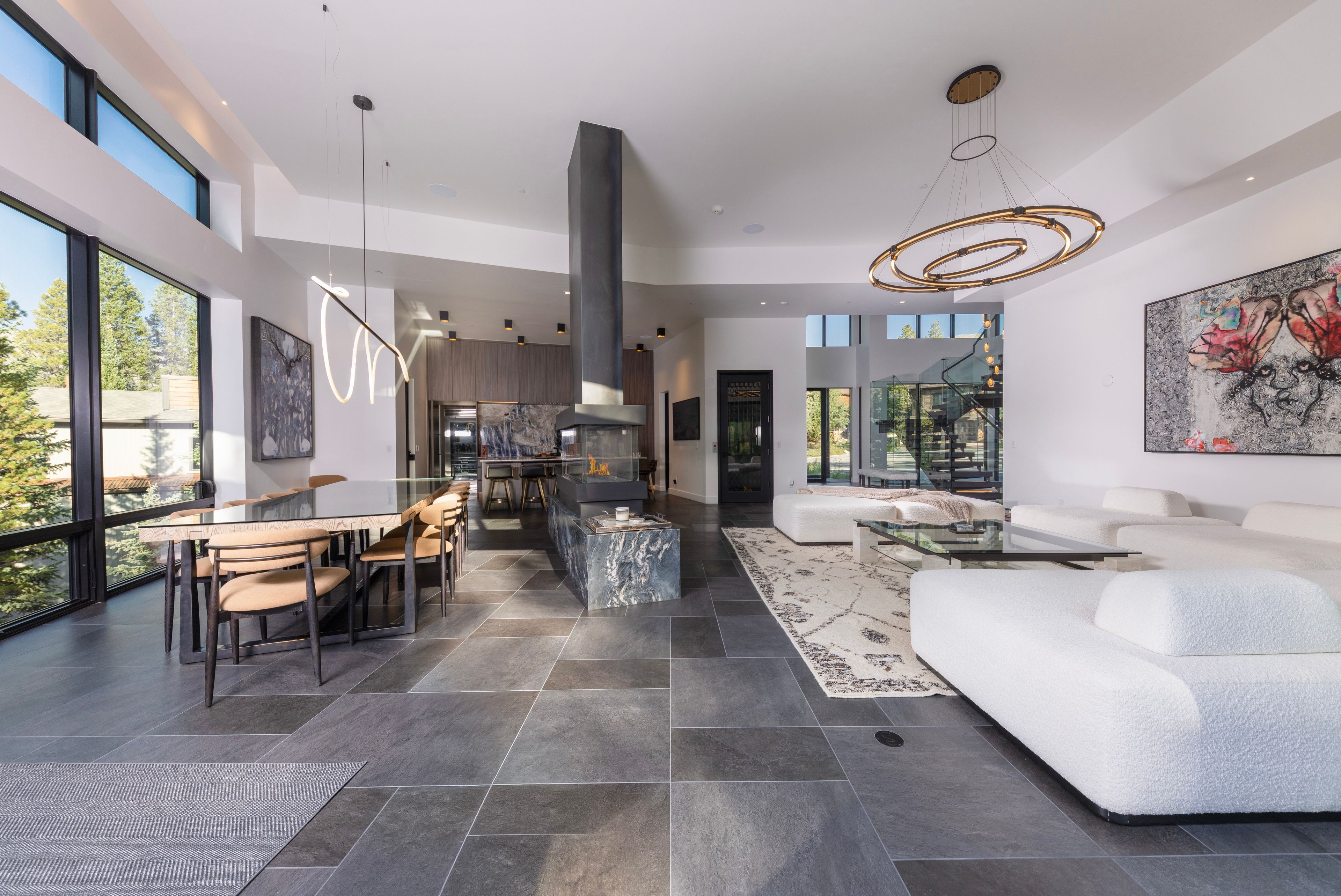 Un intérieur moderne comprenant un coin repas, une cuisine et un espace de vie, avec de grandes fenêtres et un mobilier contemporain.