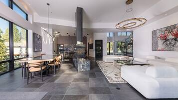 Un intérieur moderne comprenant un coin repas, une cuisine et un espace de vie, avec de grandes fenêtres et un mobilier contemporain.
