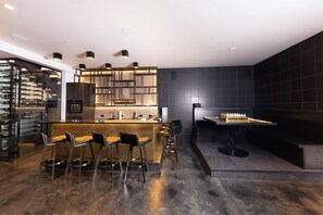 A modern bar area with a wine rack, bar stools, and a chess table. - Steps to slopes; 7,000 sq feet of Luxury, golf simulator, hot tub! (Copper Mountain)