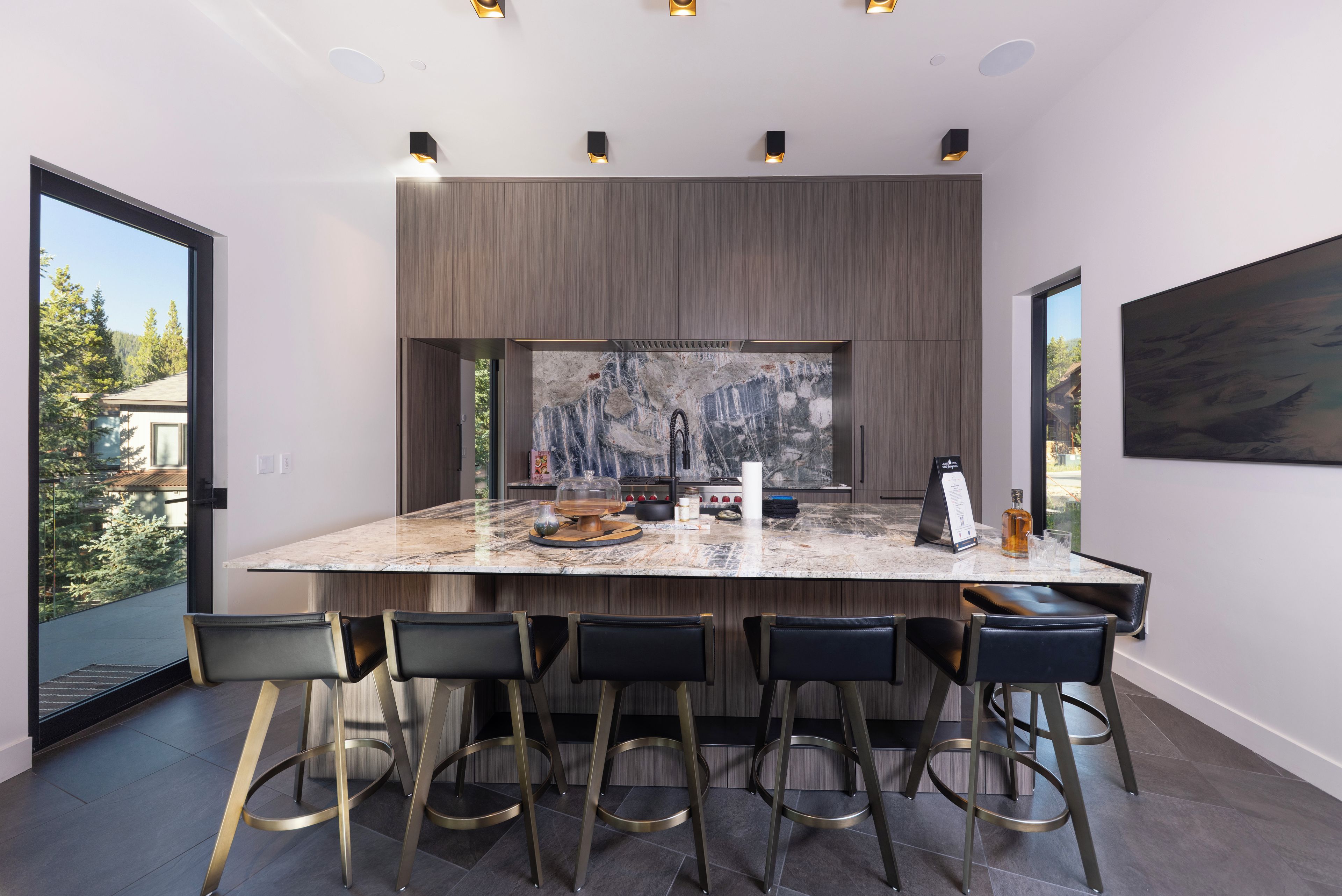 A modern kitchen with a large island, bar stools, and a view of the outdoors.