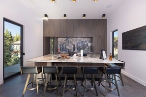 A modern kitchen with a large island, bar stools, and a view of the outdoors.