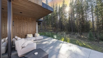 A modern outdoor living space with a sofa and a coffee table, overlooking a forested area.