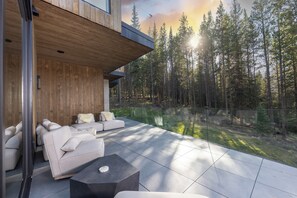 A modern outdoor living space with a sofa and a coffee table, overlooking a forested area. - Steps to slopes; 7,000 sq feet of Luxury, golf simulator, hot tub! (Copper Mountain)