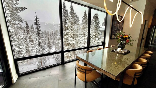 A modern dining area with a large window overlooking a snowy forest. - Steps to slopes; 7,000 sq feet of Luxury, golf simulator, hot tub! (Copper Mountain)