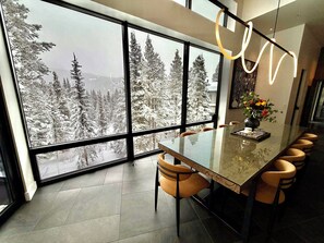 A modern dining area with a large window overlooking a snowy forest. - Steps to slopes; 7,000 sq feet of Luxury, golf simulator, hot tub! (Copper Mountain)
