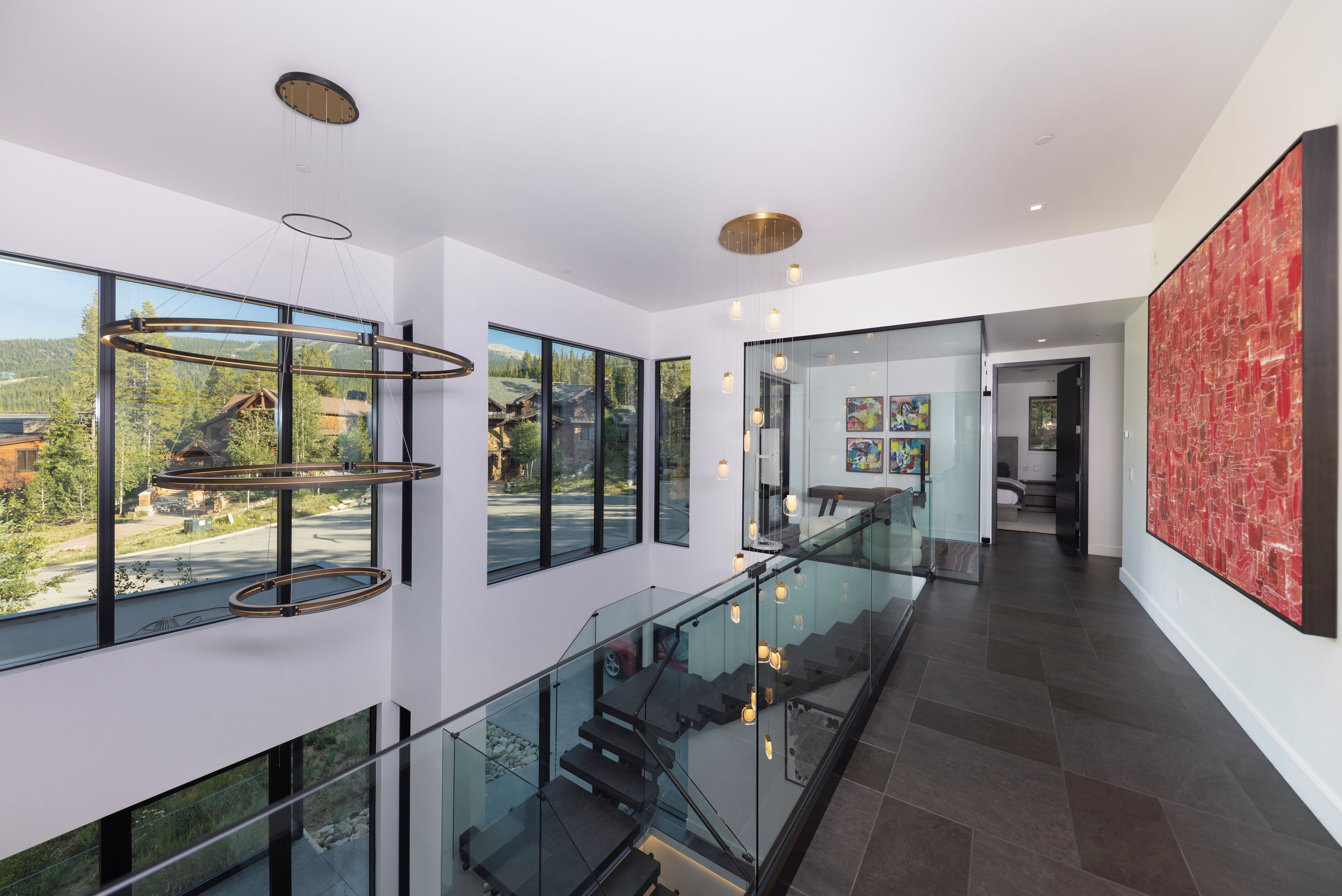 A modern interior with a glass staircase, large windows, and a view of a mountainous landscape.
