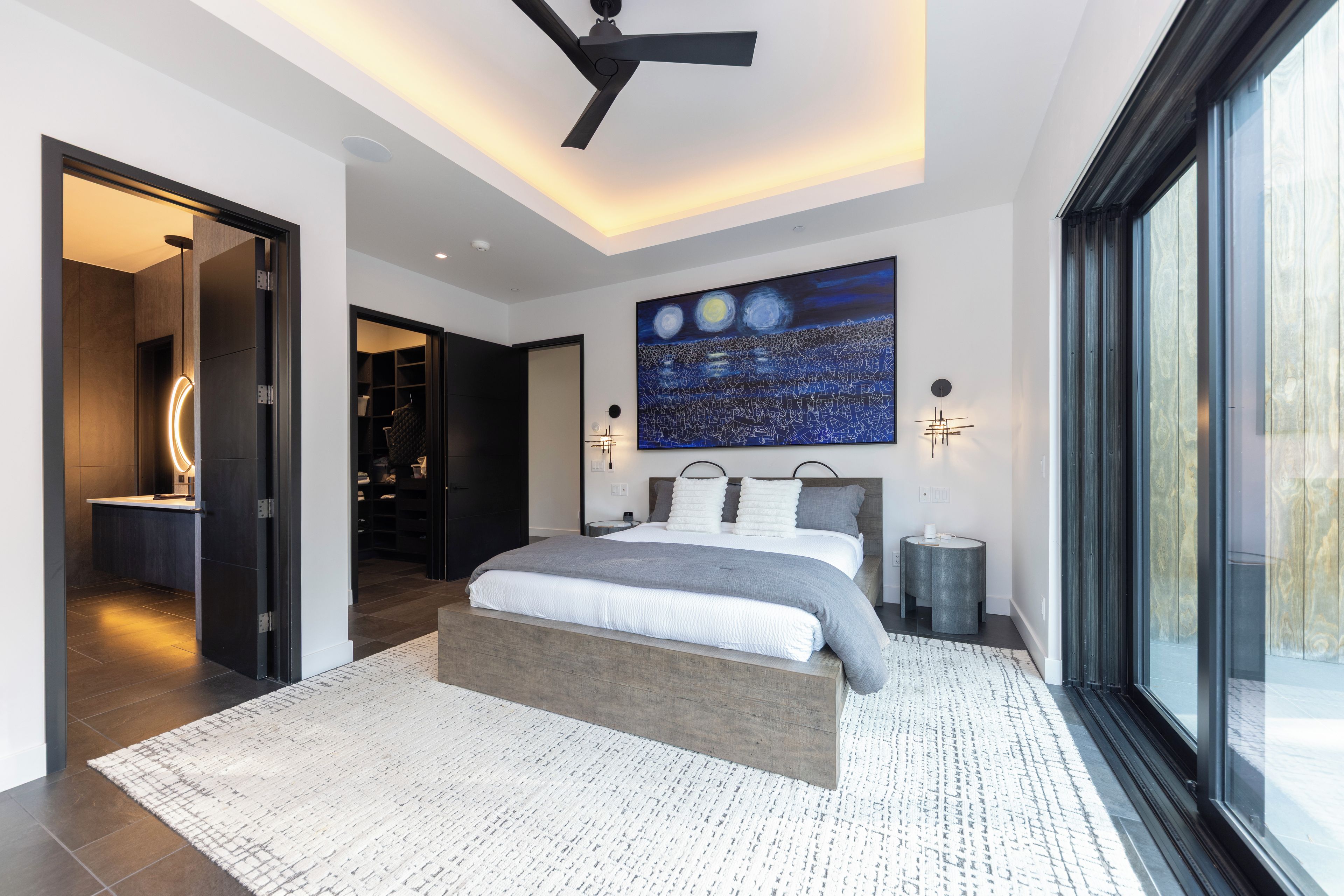 Un dormitorio moderno con una cama grande, un ventilador de techo, un tragaluz y un cuadro de paisaje urbano en la pared.