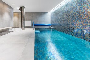 Una piscina con pared de mosaicos, un banco y zona de vestuarios.