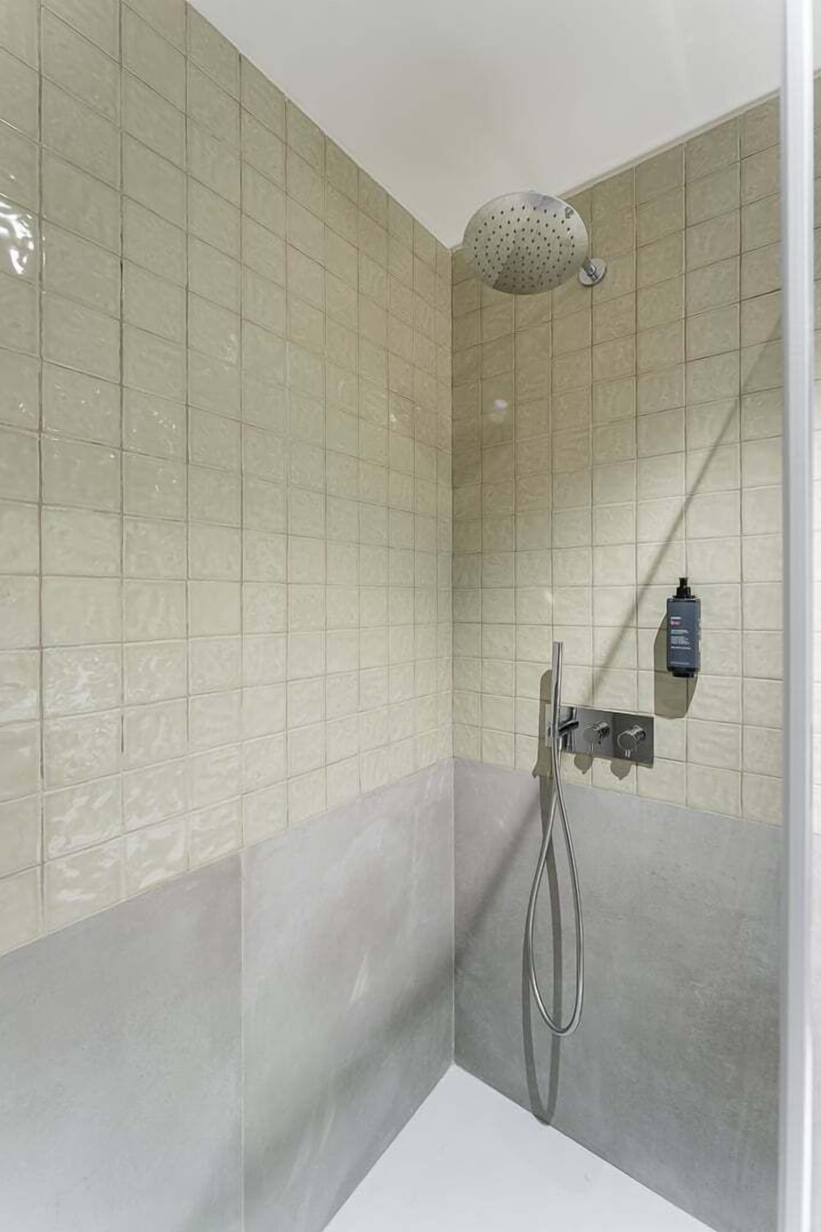 A shower with a handheld showerhead, a wall-mounted control panel, and a tiled wall.