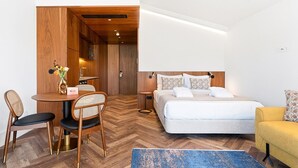 A hotel room with a bed, a desk with chairs, a small table with a vase, and a yellow armchair. - GuestReady - Santa Barbara Garden House 32 (Braga)