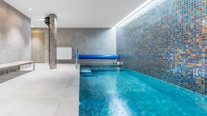 Una piscina con pared de mosaicos, un banco y zona de vestuarios.