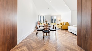 Una habitación amplia con piso de madera, un área de comedor con sillas y una mesa, un sofá amarillo y una cama.