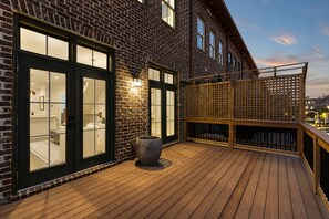 Een houten terras met een bakstenen gebouw, grote glazen deuren en een houten omheining.