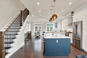 A modern kitchen with a central island, stainless steel appliances, and a staircase with wooden railings. - Luxury Riverfront Retreat in the Eastern Wharf | Heated Pool Access (Savannah)