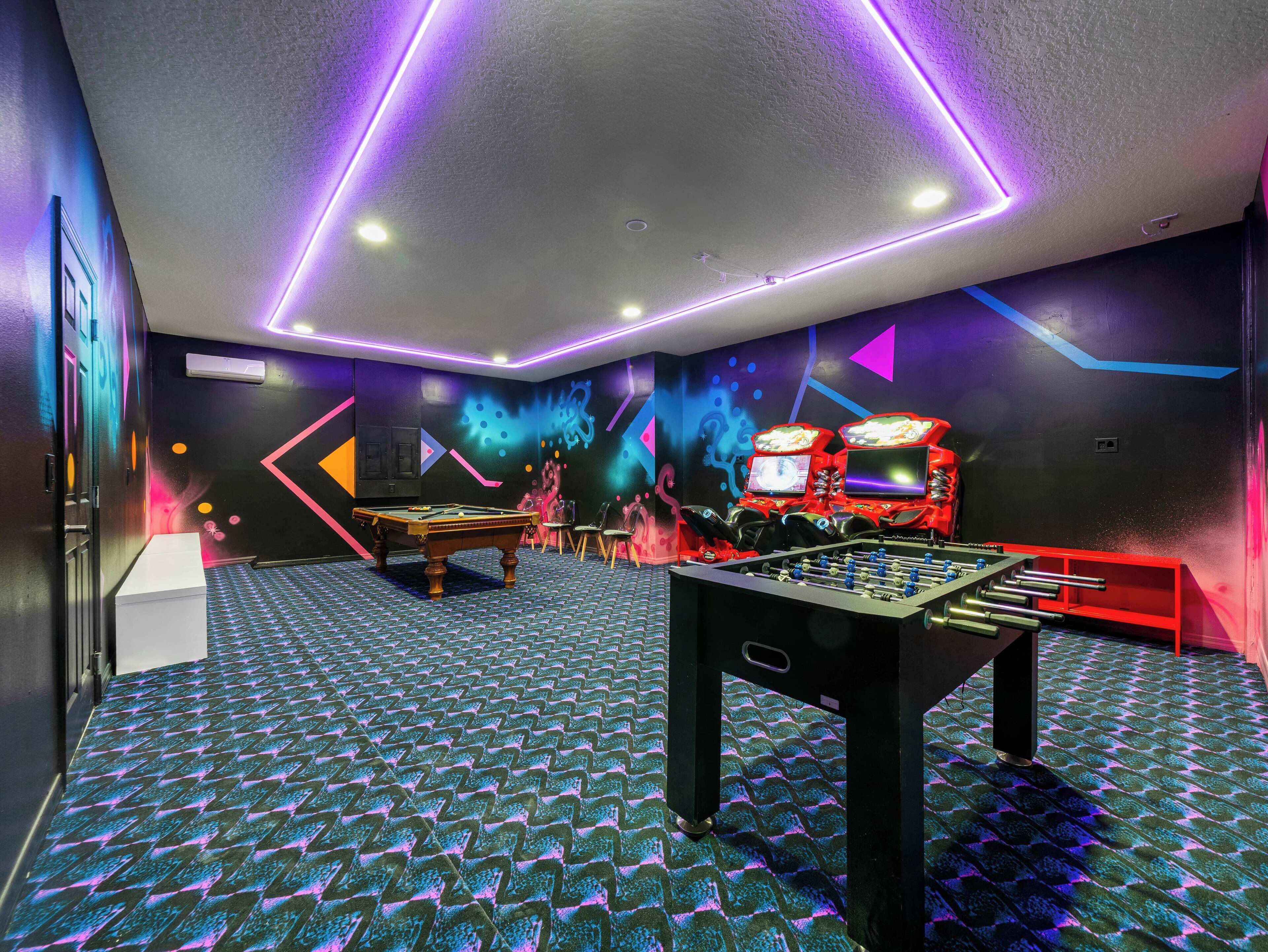 A room with a pool table, foosball table, and a wall with colorful graffiti.