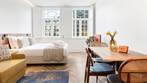 Ein modernes Hotelzimmer mit einem Bett, einem Sofa, einem Esstisch mit Stühlen und großen Fenstern.